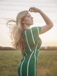 Young woman with arms raised standing on field against sky