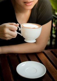 Midsection of woman holding coffee cup on table