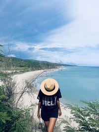 Rear view of young woman standing by sea against sky