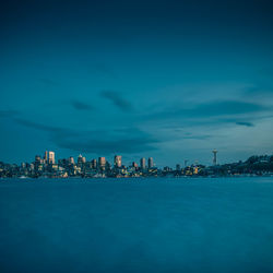 Sea by illuminated buildings against blue sky