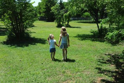 Rear view of women standing on grass against trees