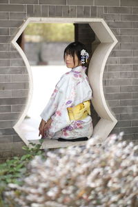Rear view portrait of young woman wearing kimono while sitting in window