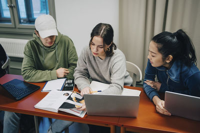 High angle view of students studying while sitting with laptop at desk in school