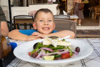 Portrait of boy sitting by table at restaurant