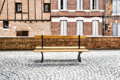 Empty bench on sidewalk by buildings in city
