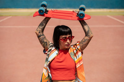 Caucasian girl with tattoos and short black hair on a sports ground with a skateboard in her hands