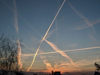 Low angle view of vapor trails in sky at sunset