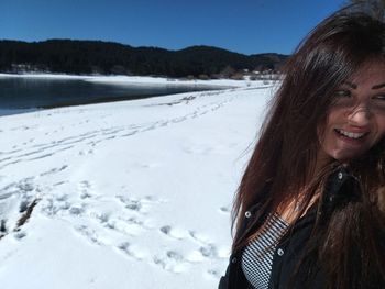 Smiling woman standing on snow covered field against clear sky