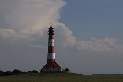 Lighthouse on field by building against sky