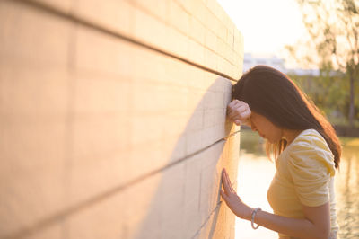 Side view of young woman standing against wall