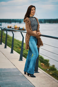 Young woman standing on railing against water
