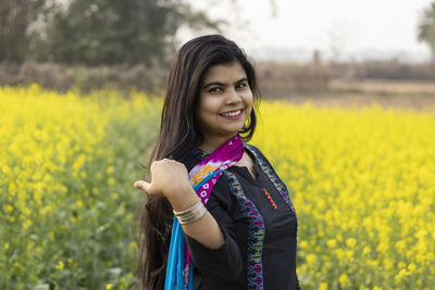 A pretty indian woman with smiling face touching hair in mustard field