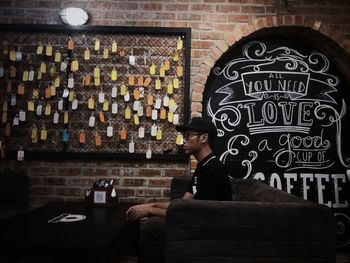 Side view of young man sitting by wall in cafe