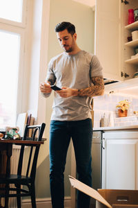 Mid adult man using mobile phone while standing by dining table at new home