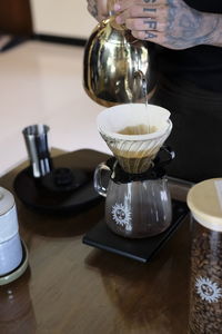 Midsection of person pouring coffee in cup on table