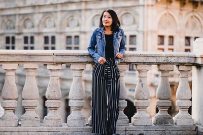 Portrait of young woman standing against railing