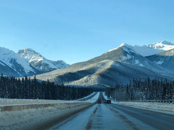 Road amidst snowcapped mountains against clear sky