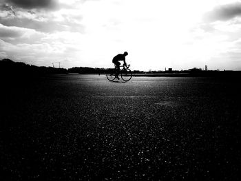 Silhouette man riding bicycle on road against sky