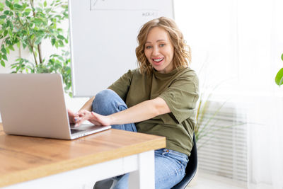 Portrait of smiling young woman using phone while sitting on table