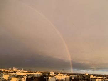 Rainbow over city buildings against sky at sunset