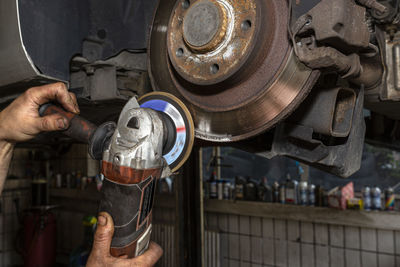 A mechanic grinds, with an angle grinder, the edge of an old rear brake disc in a car.