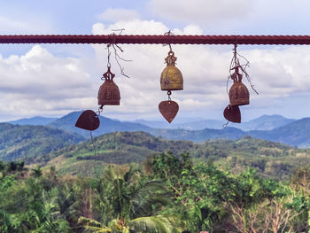 Buddhist golden bell hanging on a wire tied to a metal rod. mountains are in the background. 