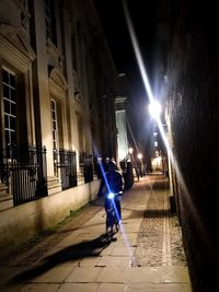 Man walking on illuminated street amidst buildings at night