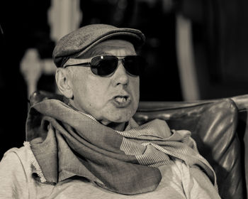 Close-up of senior man in sunglasses and cap making face while sitting on chair