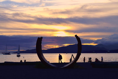 Silhouette people on beach against sky during sunset