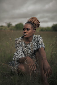 Young man sitting on field against sky