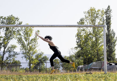 Side view of man jumping on field against sky