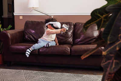 Cute boy wearing virtual reality simulator while sitting on sofa at home