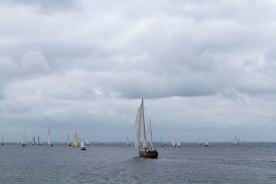 Sailboats in sea against cloudy sky