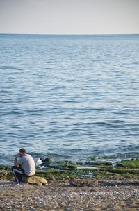 Man sitting by sea against sky