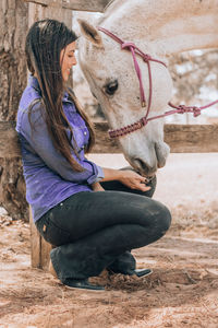 Smiling young woman feeding horse at ranch