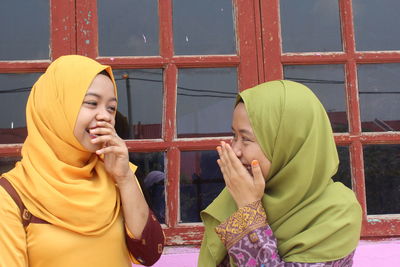 Happy female friends standing by window