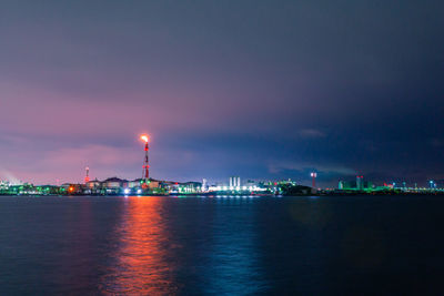 Illuminated cityscape by sea against sky at night