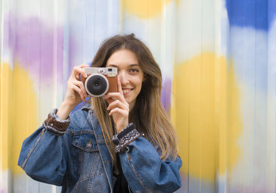 Portrait of smiling woman holding camera against curtain