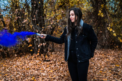 Young woman holding distress flare while standing in forest during autumn