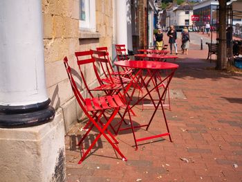 Red chairs and table at sidewalk cafe by street in city