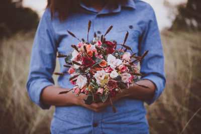 Midsection of woman holding bouquet on field