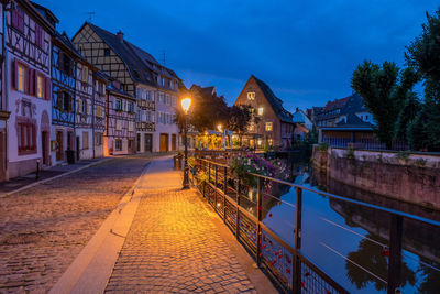 Illuminated street amidst buildings against sky at night