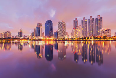 Reflection of illuminated buildings in river against sky during dusk