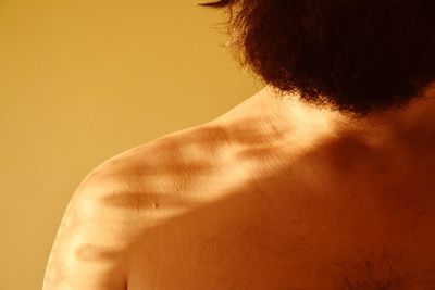 Rear view of shirtless man against yellow background