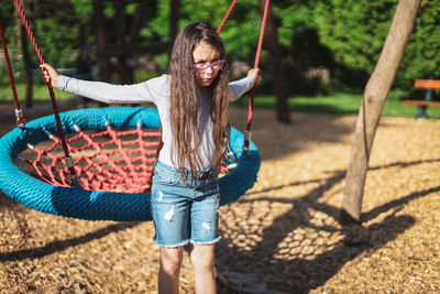 Portrait of a beautiful caucasian dissatisfied girl with a round rope swing in the park