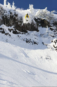 Person skiing off a big cliff to a snow covered land