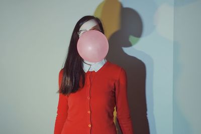 Woman blowing bubble gum while standing against wall