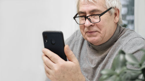 Hoary old man looking at web camera, holding phone, talking with children, wife online. senior