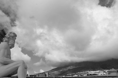 Side view of young man sitting on mountain against sky