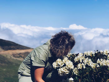 Side view of woman smelling flowers in field against sky